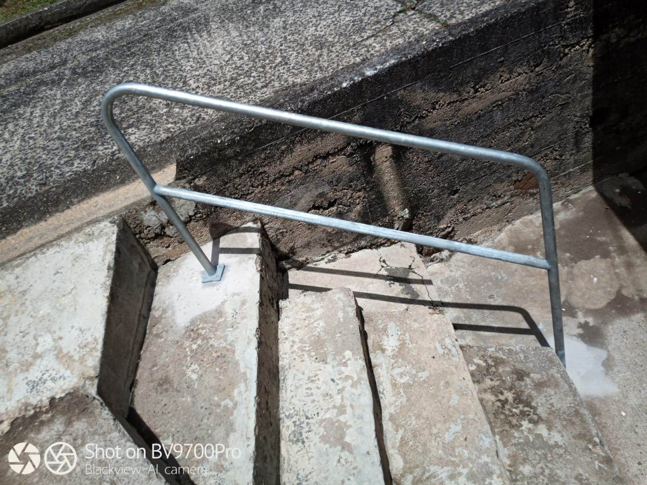Une rampe métallique fixée à un escalier extérieur en béton.