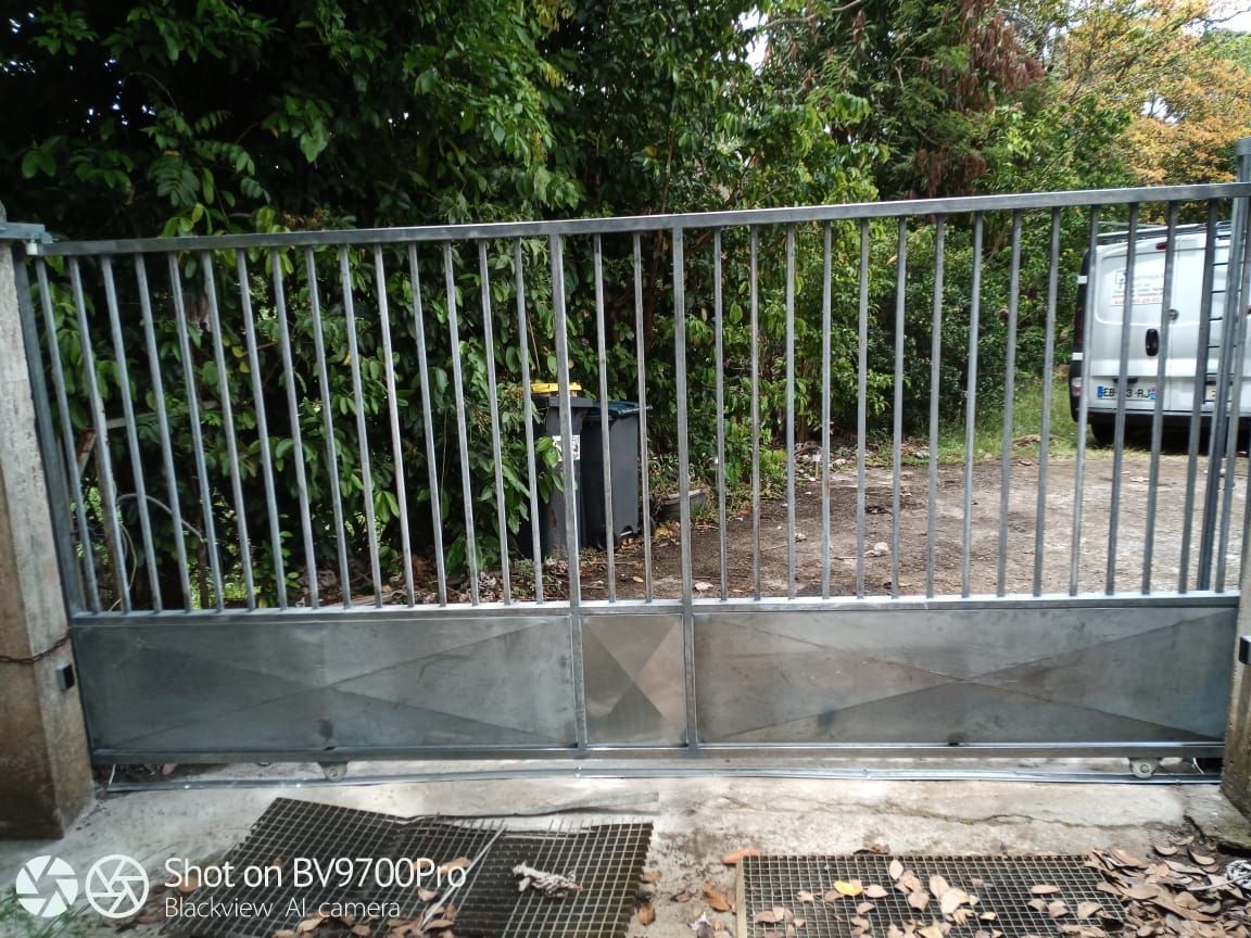 Un portail d'allée en métal gris, avec des barreaux verticaux en haut et des panneaux métalliques pleins en bas.