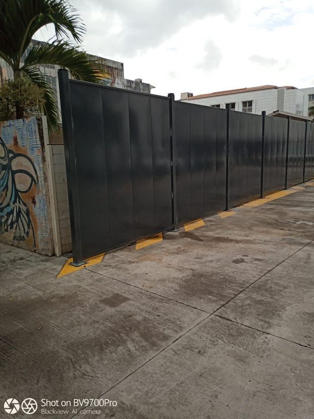 Une clôture noire opaque se dresse sur un terrain en béton.