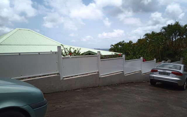 Une clôture blanche à panneaux étagés surplombe un mur en béton.
