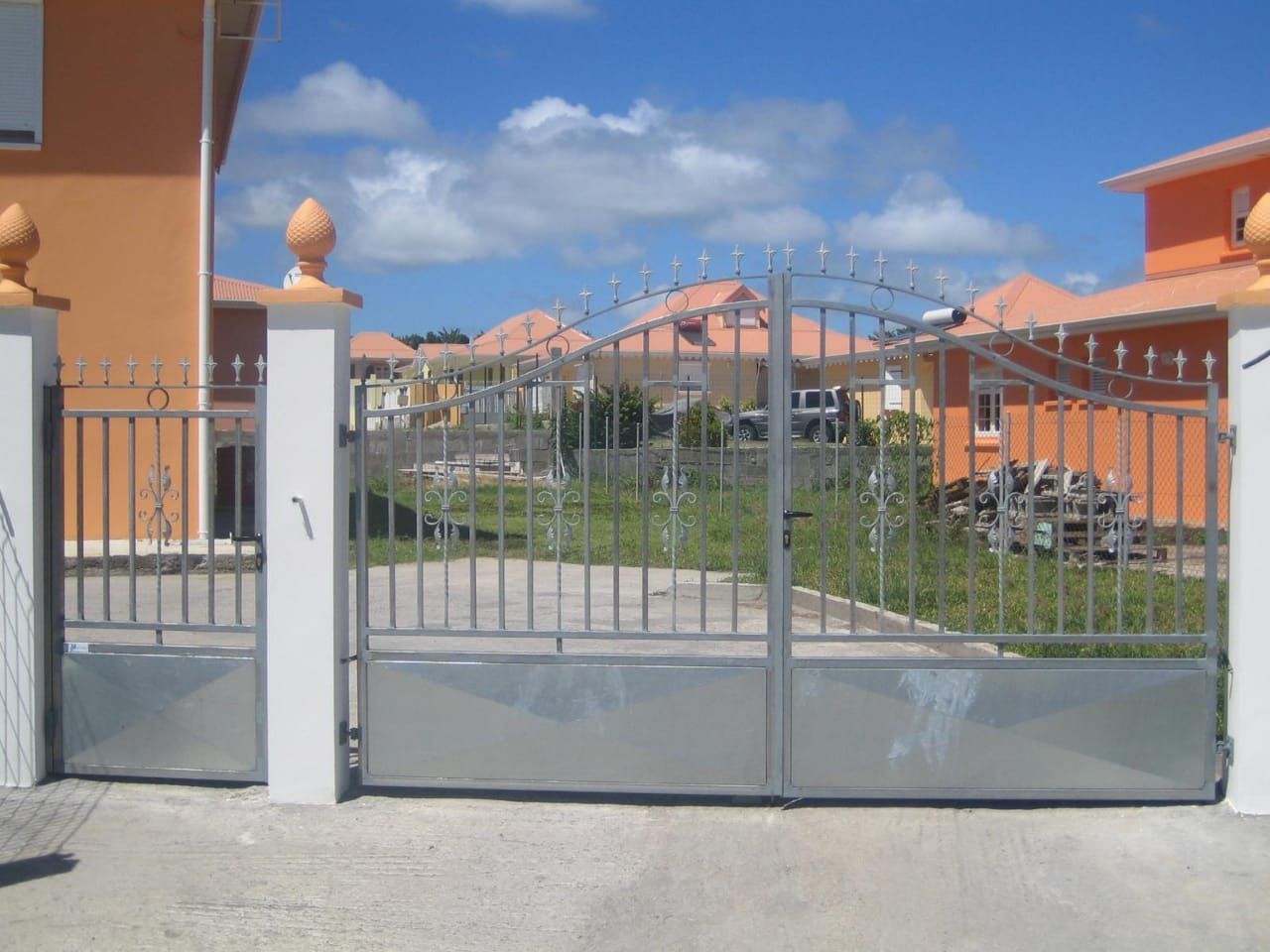 Un portail en métal gris entre des piliers en béton blanc.