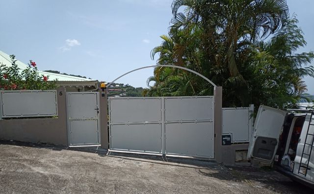 Un portail d'allée blanc avec une arche métallique décorative et un portillon piéton assorti.
