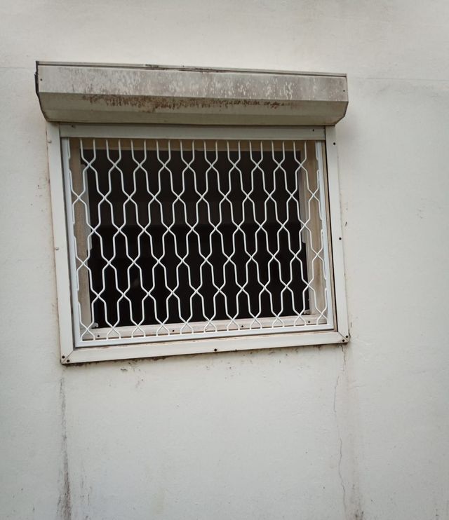 Une fenêtre rectangulaire sur un mur blanc, équipée d'une grille de sécurité en métal blanc.