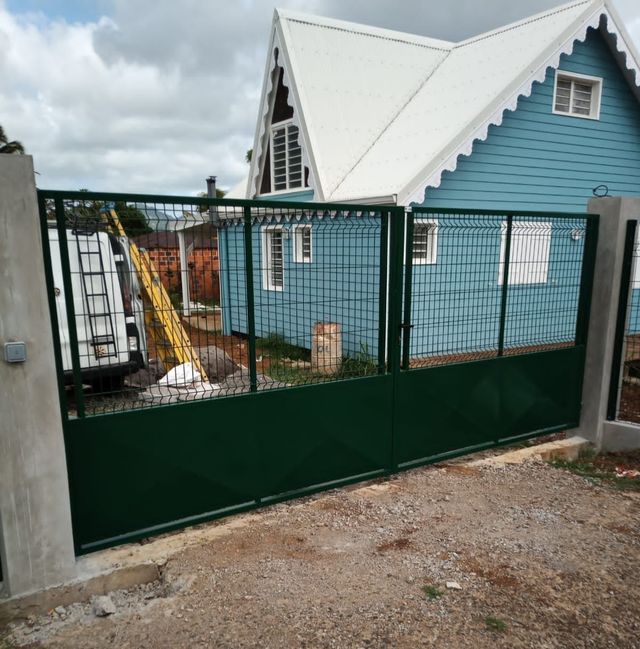 Un portail métallique vert, orné de panneaux en treillis métallique.