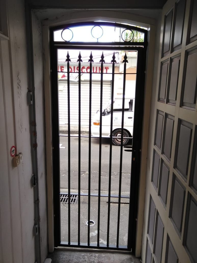 Une grille de protection en métal noir à barreaux pointus, vu depuis une porte intérieure.