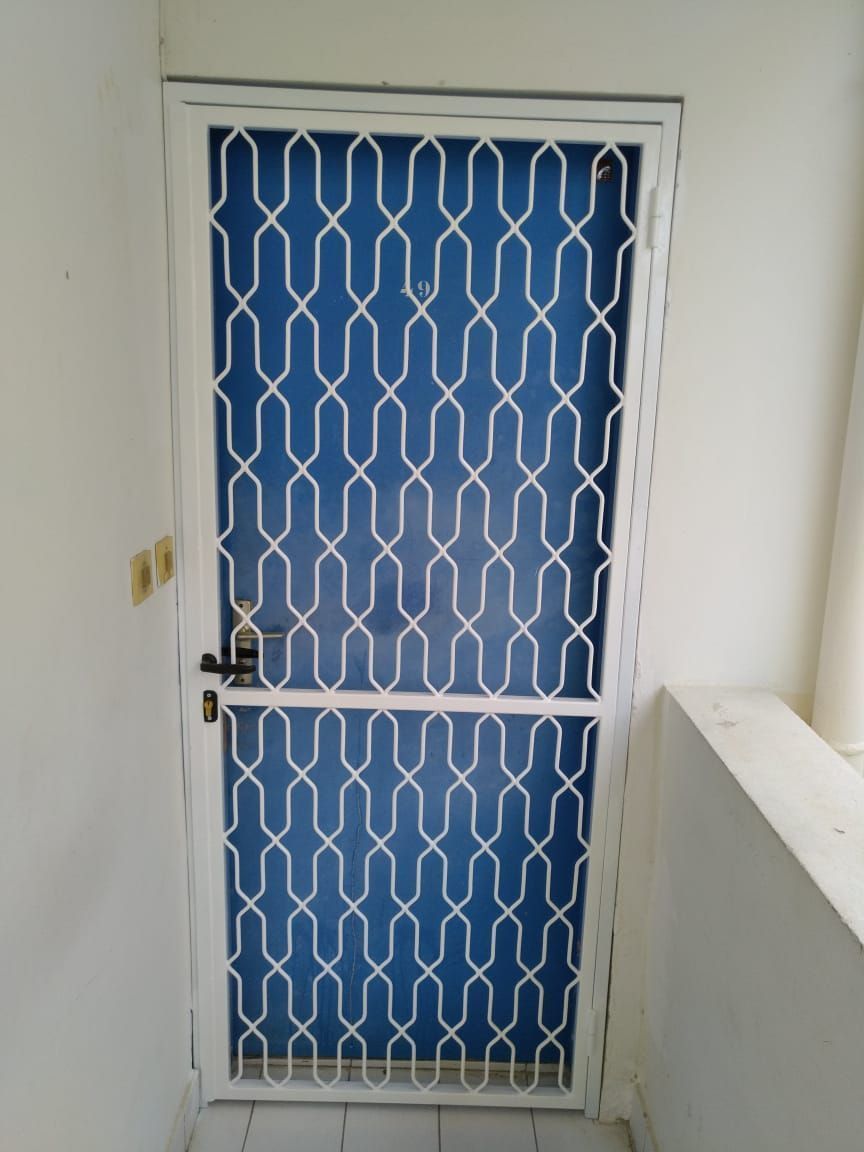 Une porte bleue recouverte d'une grille de protection en métal blanc à motif géométrique.