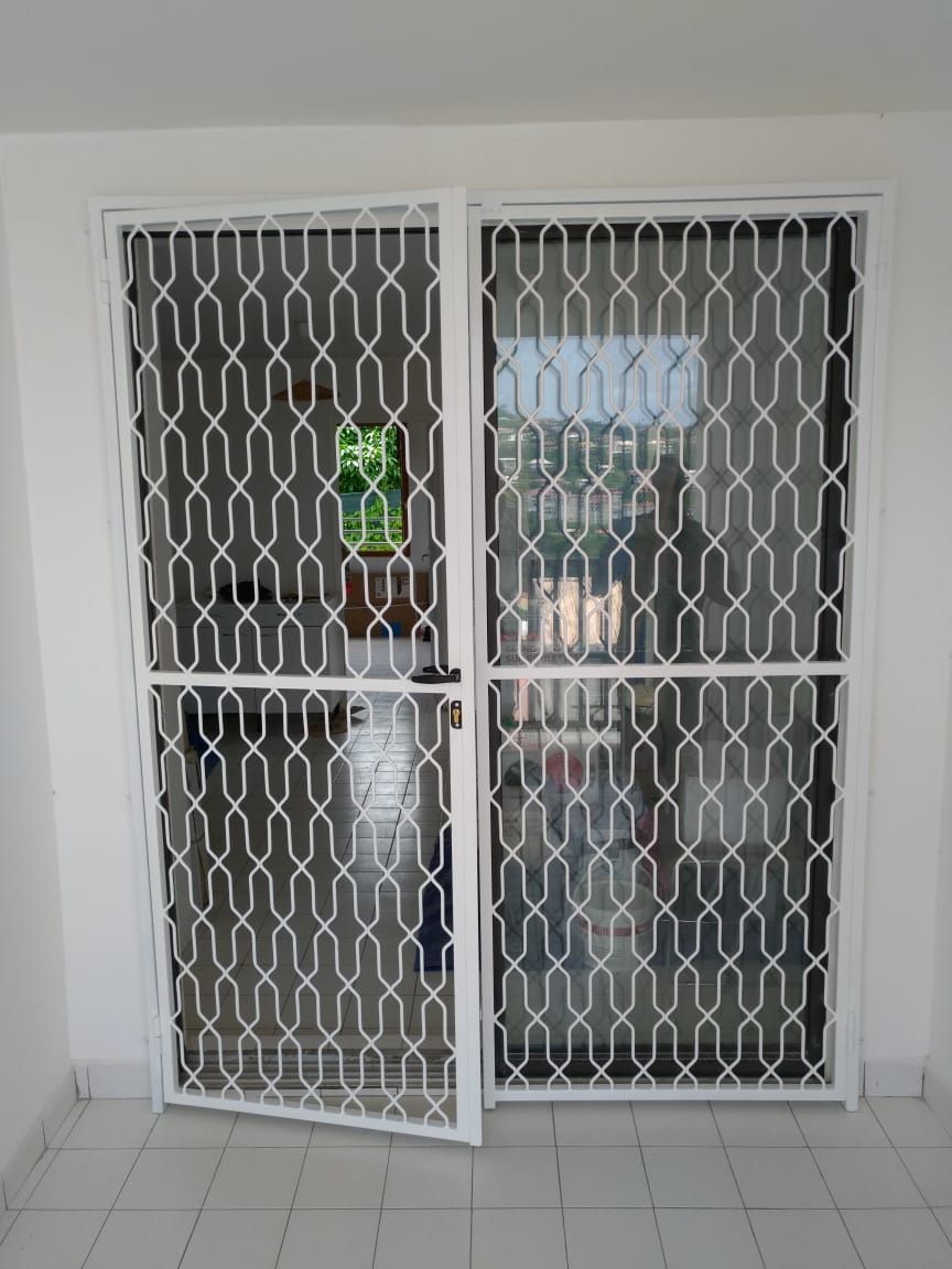 Une grille de sécurité en métal blanc à mailles losanges, installées devant une porte.