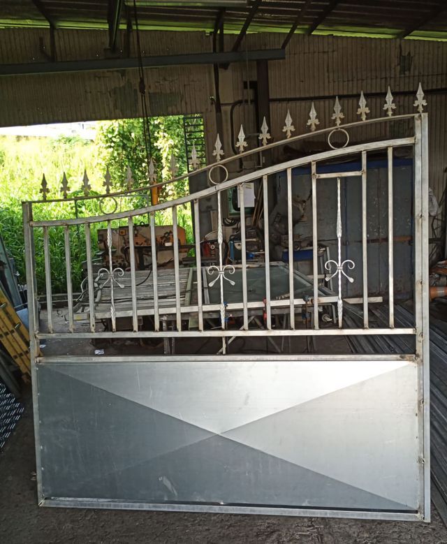 Un portail métallique composé d'un panneau en tôle pleine et d'une partie supérieure ornée de barres verticales.