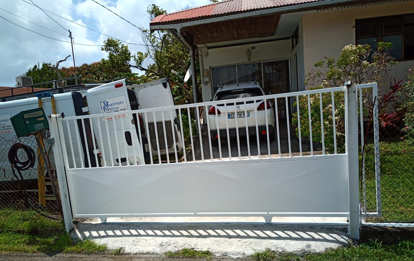 Un portail coulissant en métal blanc se dresse devant une maison d'habitation.