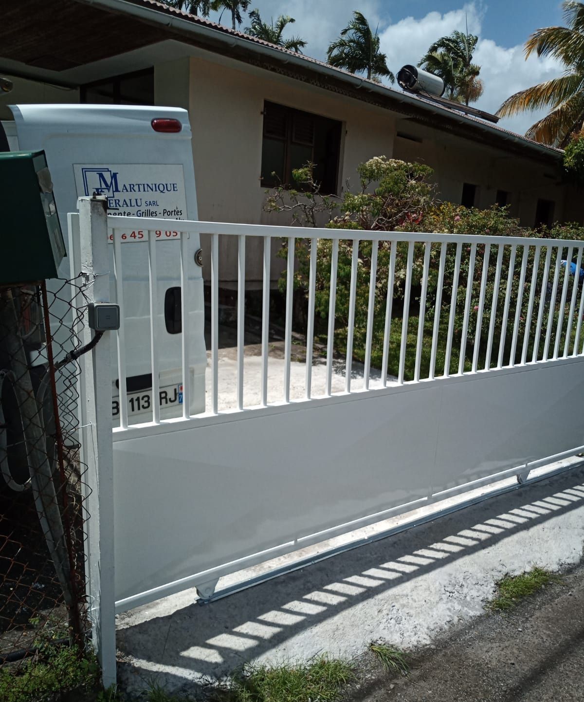 Un portail coulissant en métal blanc se dresse devant une maison d'habitation.