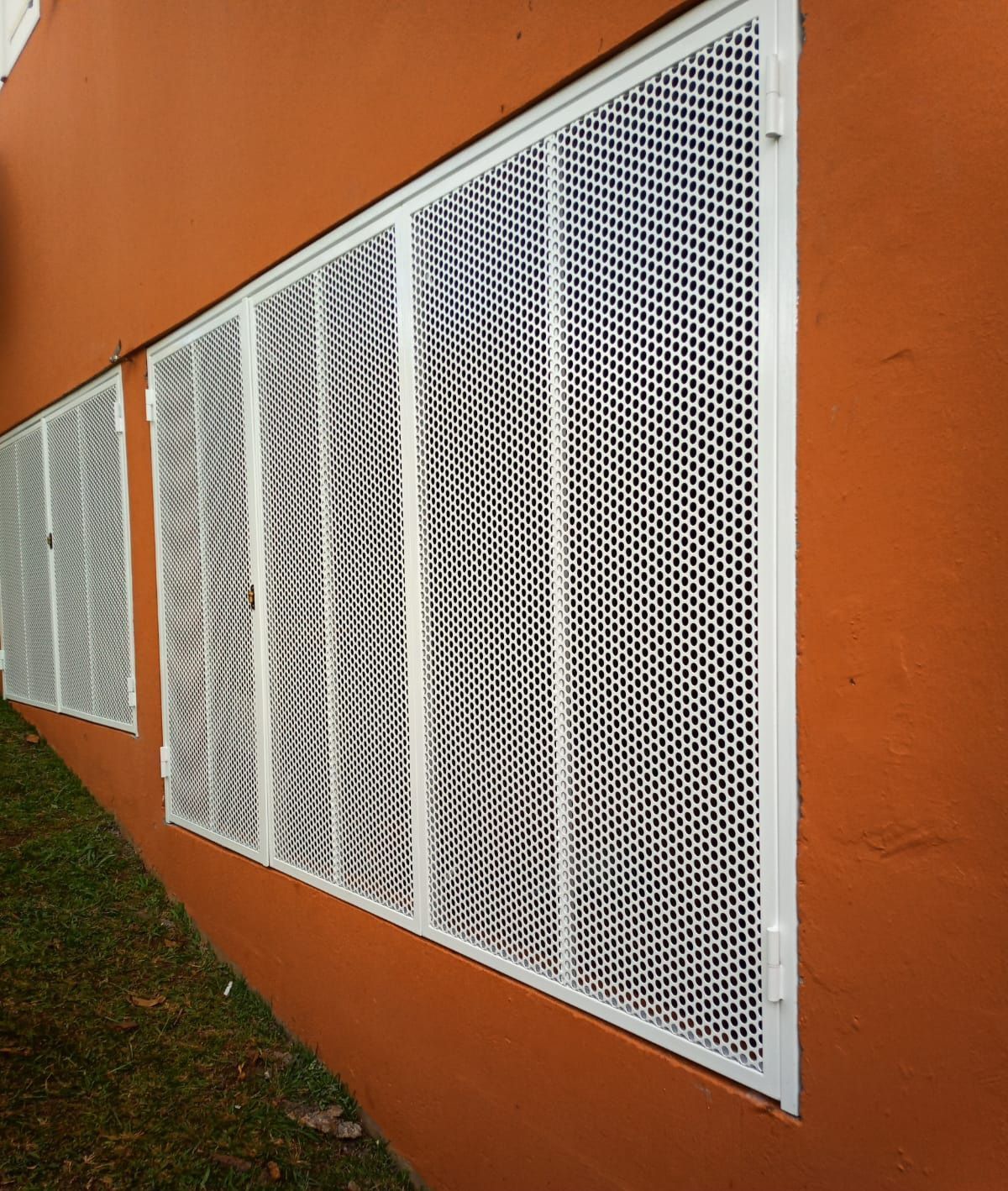 Grilles de sécurité en métal blanc à mailles losanges installées sur les fenêtres.