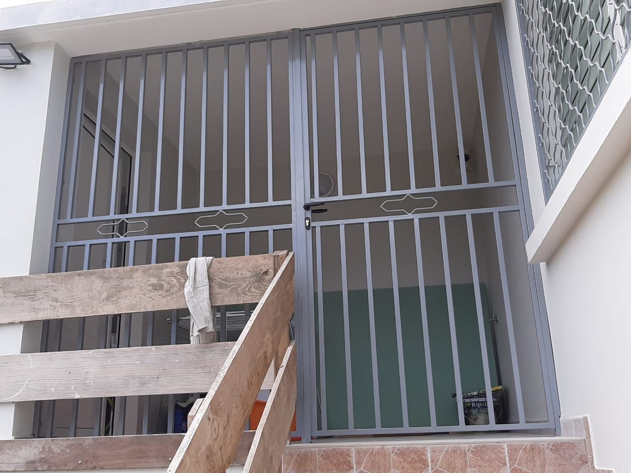 Une grille de protection en métal gris installé dans une entrée extérieure.