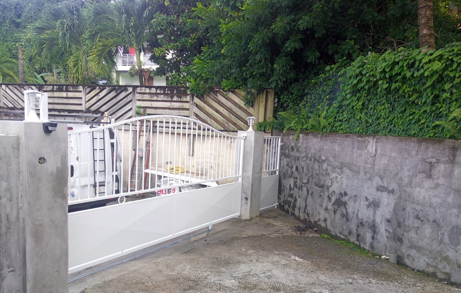 Un portail d'allée en métal blanc, encadré par deux piliers en béton.