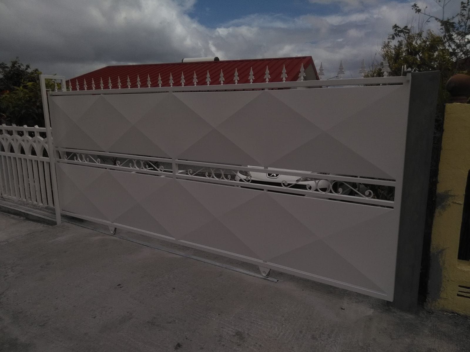 Un portail coulissant moderne en métal blanc orné d'un motif en losanges et d'une découpe horizontale décorative au centre.