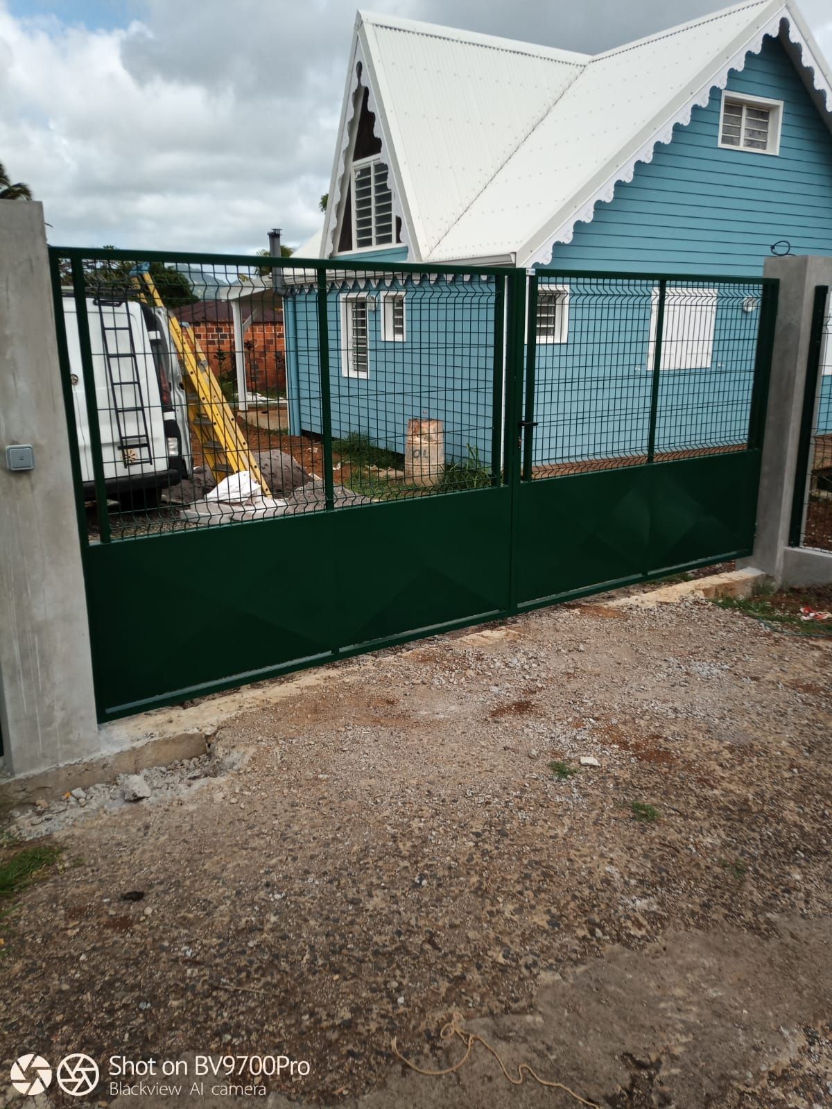 Un portail métallique vert installé devant une maison bleue au toit blanc.