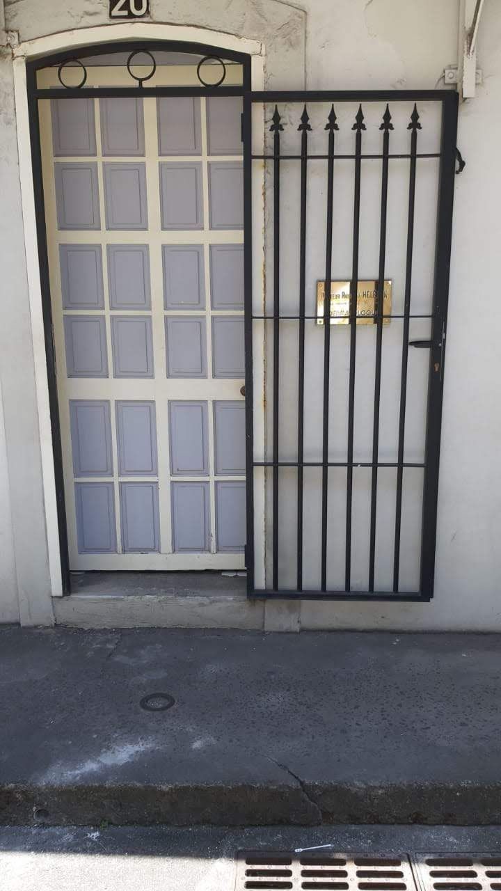 Une porte blanche à carreaux se dresse derrière une grille de sécurité en métal noir ouverte.