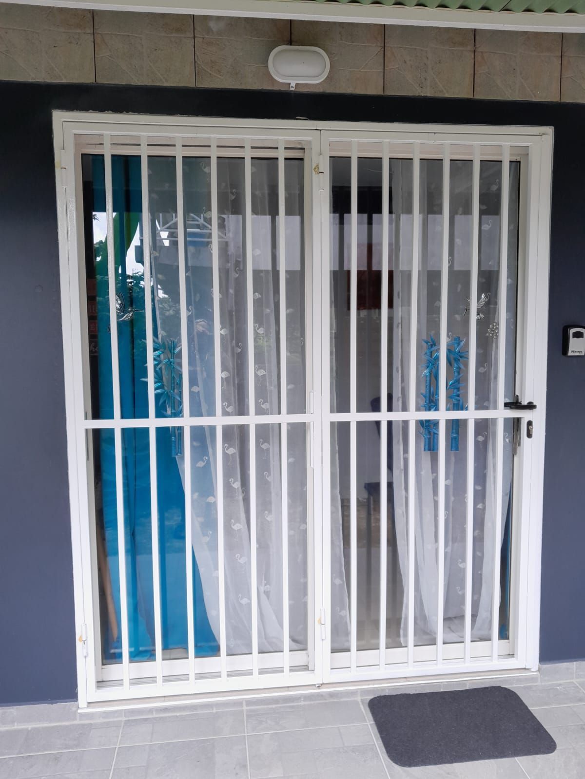 Une grille de sécurité en métal blanc recouvre une porte coulissante en verre.