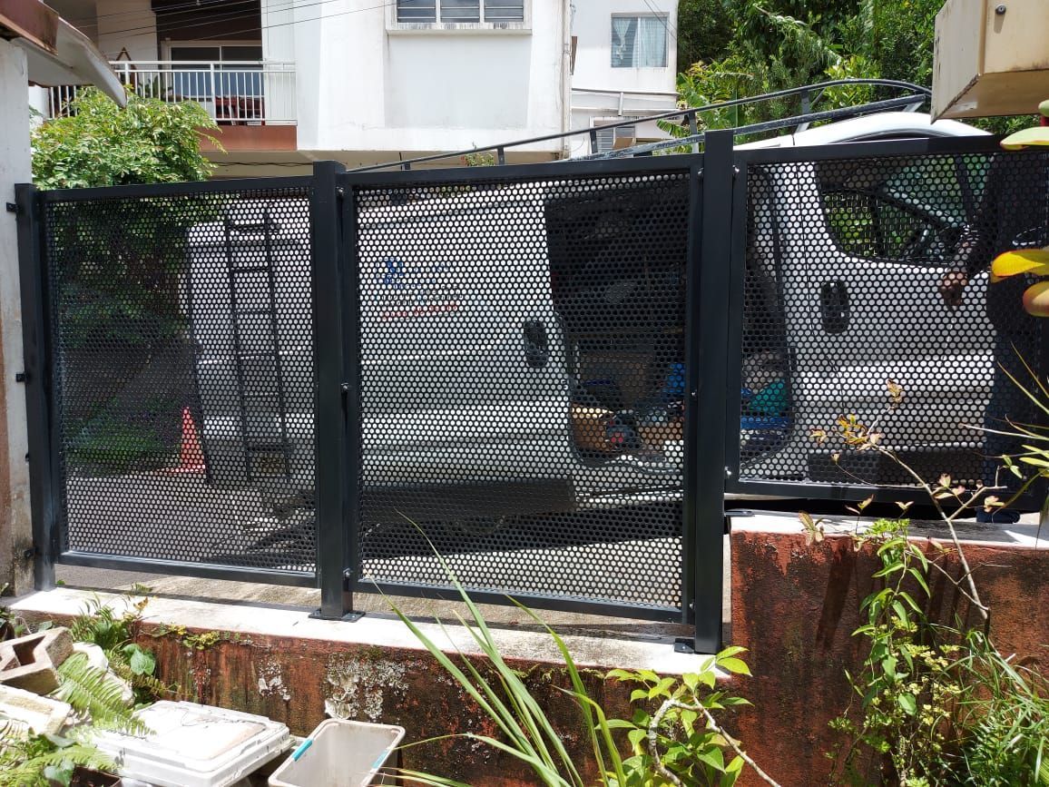 Une camionnette blanche garée derrière une clôture métallique noire en grillage, devant une maison.