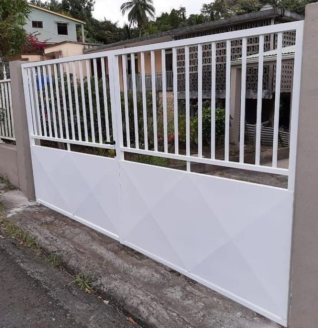 Un portail en métal blanc, avec des barreaux verticaux en partie supérieure et des panneaux à motif en partie inférieure.