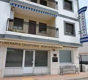 Un gran edificio blanco con un balcón y un banco delante.