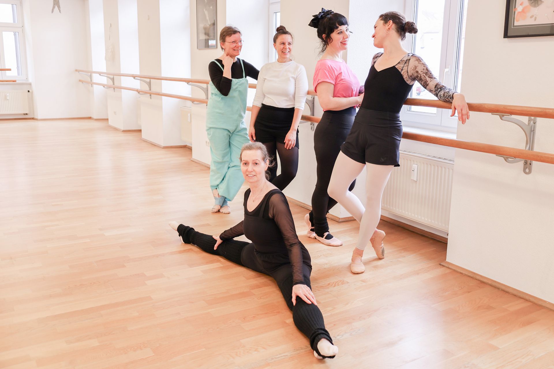 Balletttänzerinnen in schwarzen Trikots und weißen Röcken dehnen sich an der Ballettstange in einem Studio.