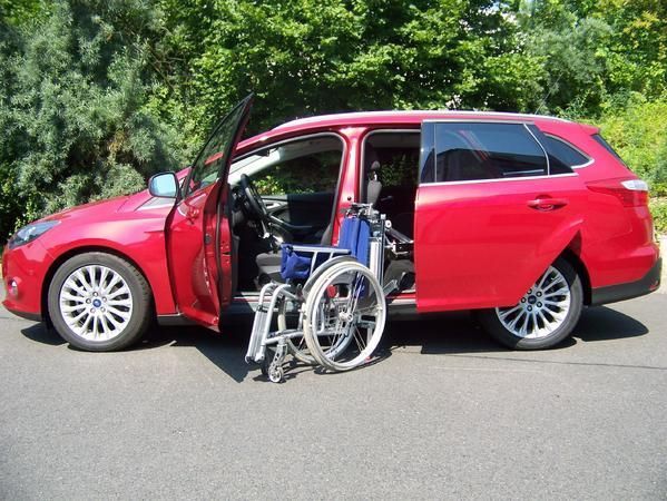 Person im Rollstuhl vor einem Pkw