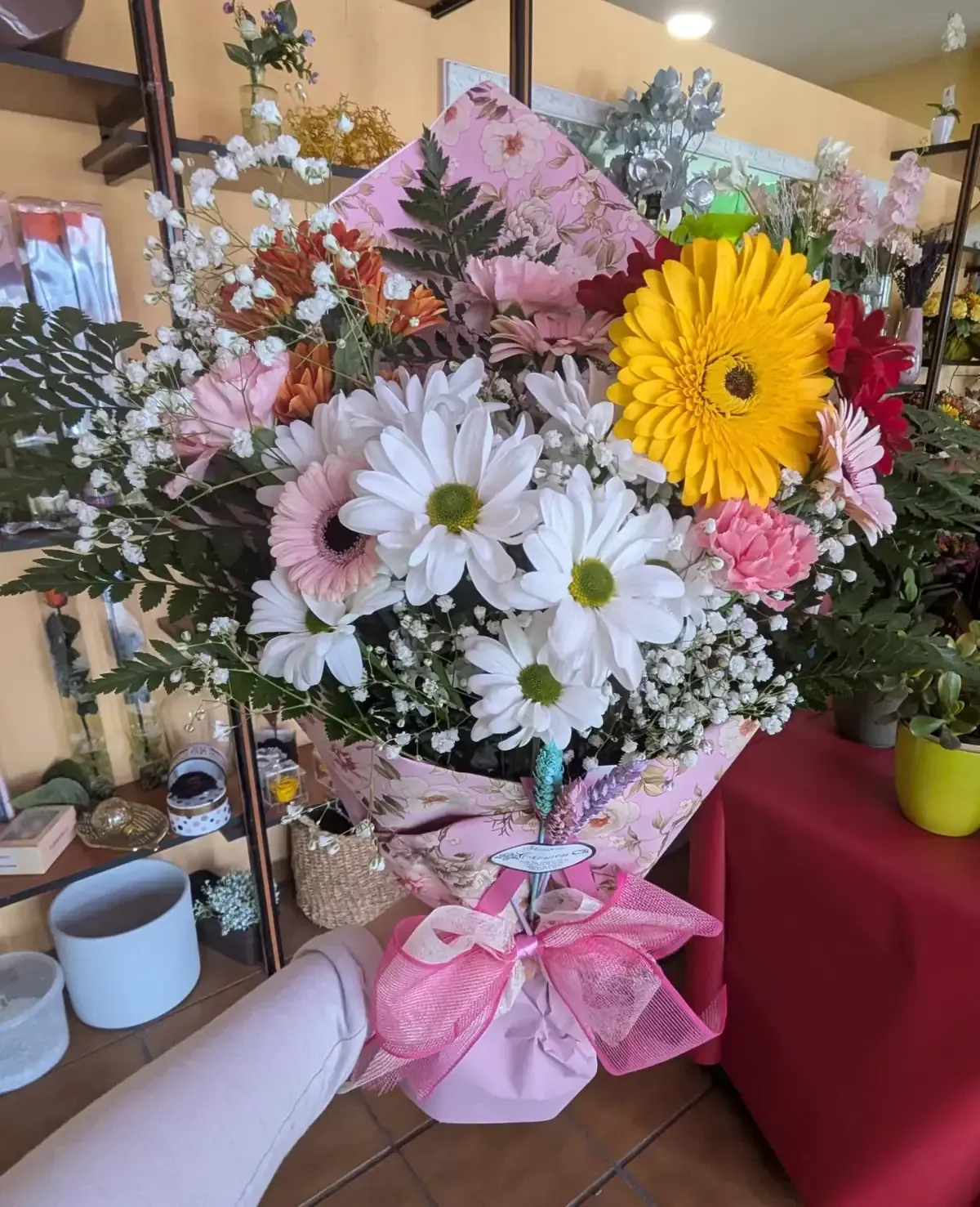 Ramo de flores rosas, blancas y amarillas atado a mano, envuelto en papel rosa con una cinta, colocado en el interior.