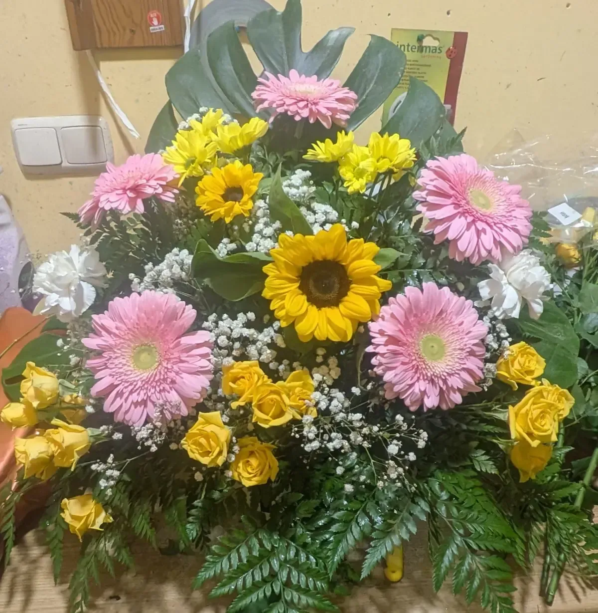 Arreglo floral colorido con margaritas rosas, rosas amarillas, girasoles y follaje verde.