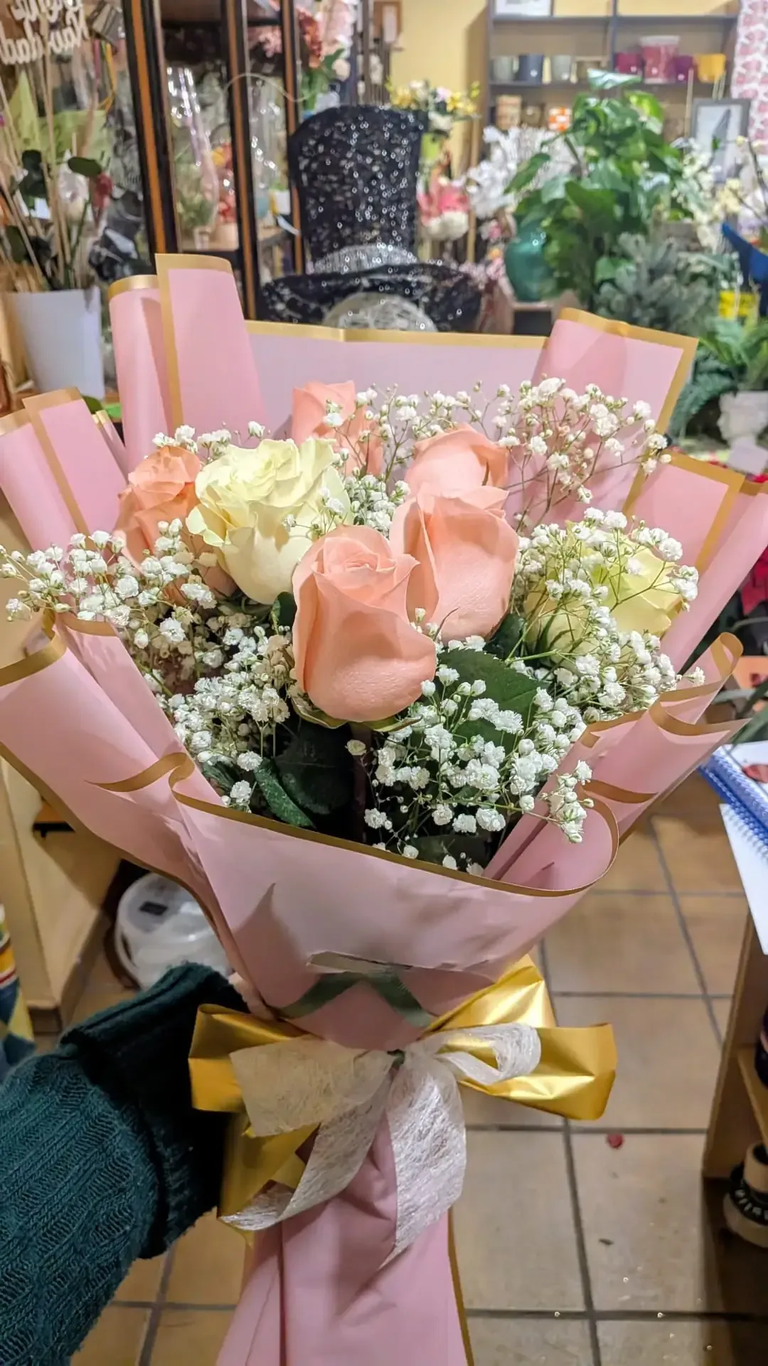 Ramo rosa y crema con rosas y paniculata, envuelto en papel y cinta de tonos pastel en una floristería.
