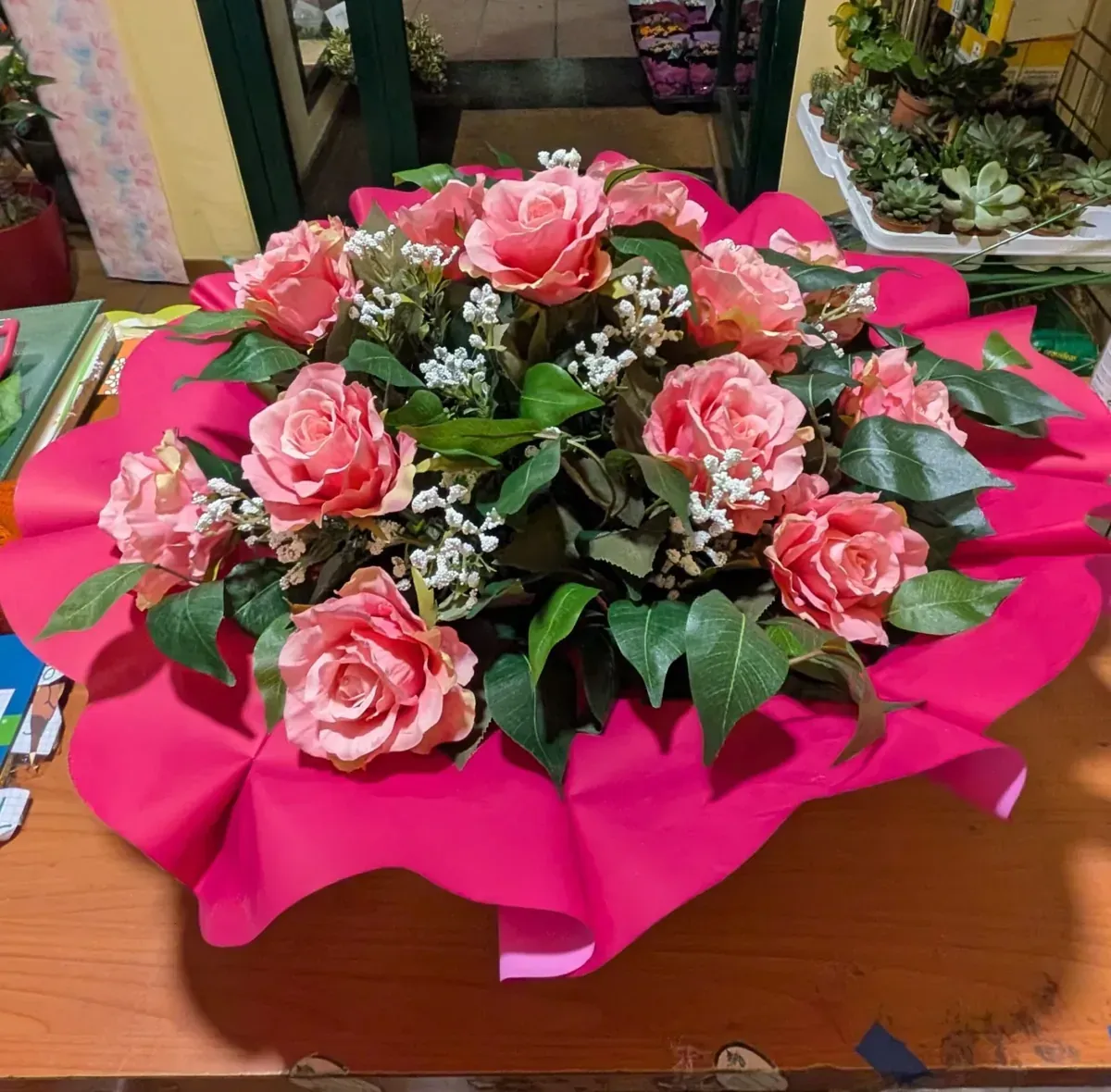 Un ramo de rosas rosadas sobre una mesa de madera, envuelto en papel rosa 