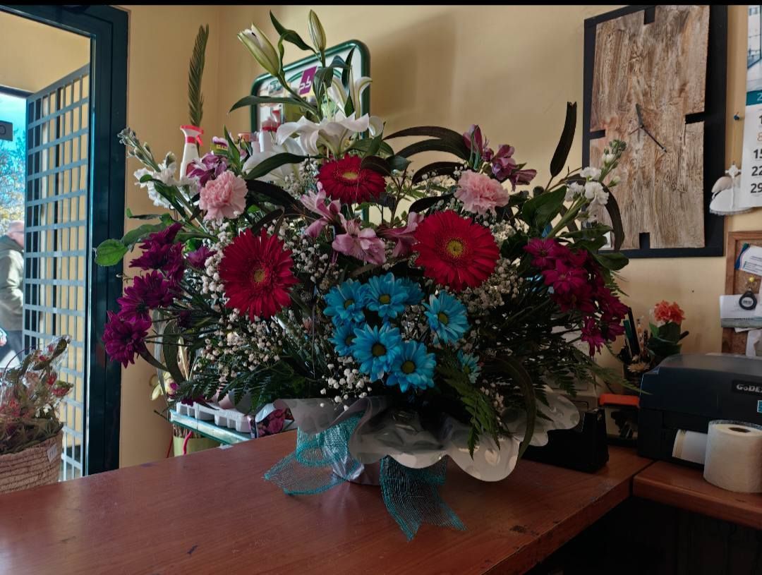 Gran ramo de flores rosas, azules y blancas en un jarrón sobre una mesa de madera en el interior.