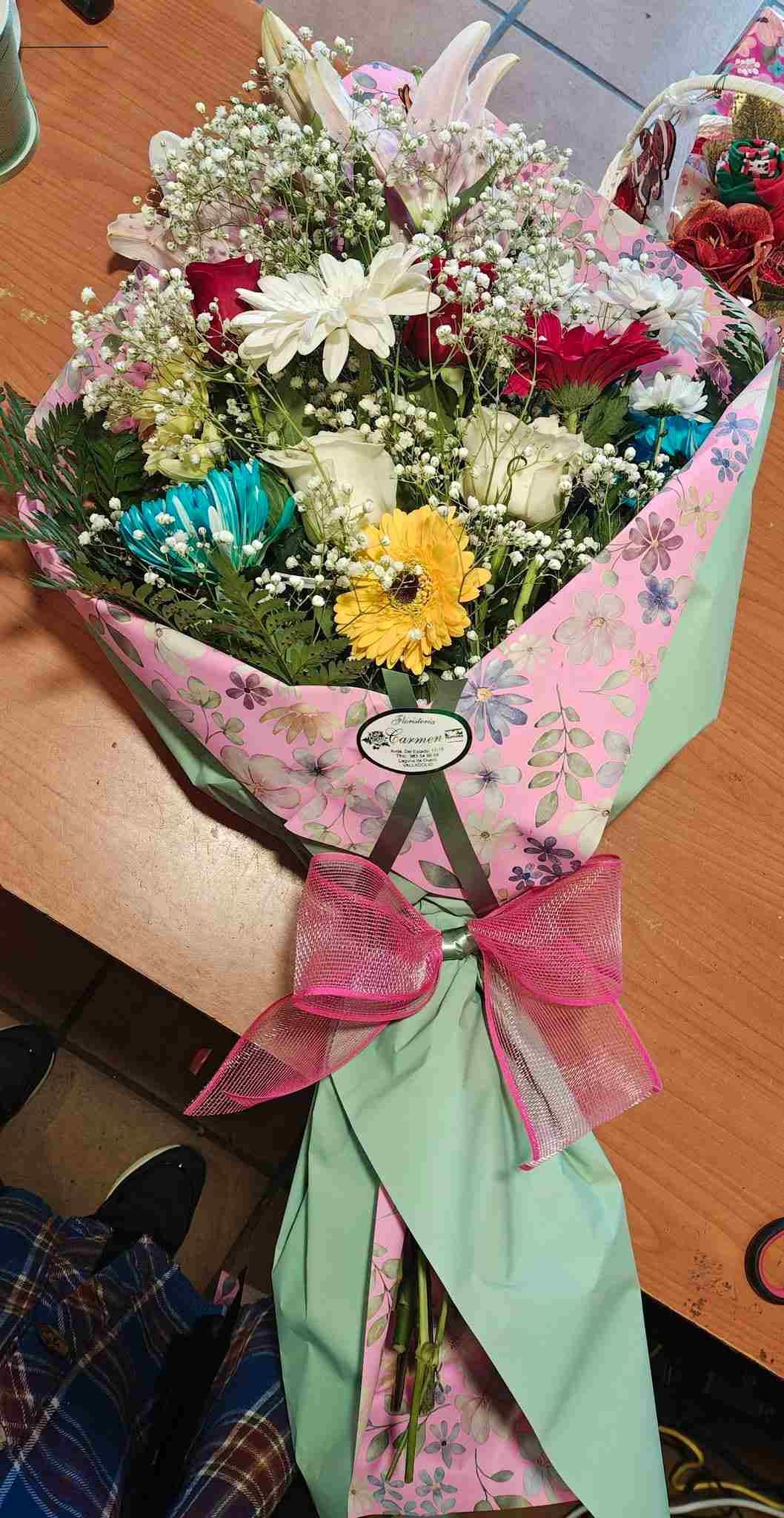 Colorido ramo de flores variadas envuelto en papel rosa con un lazo de cinta verde.