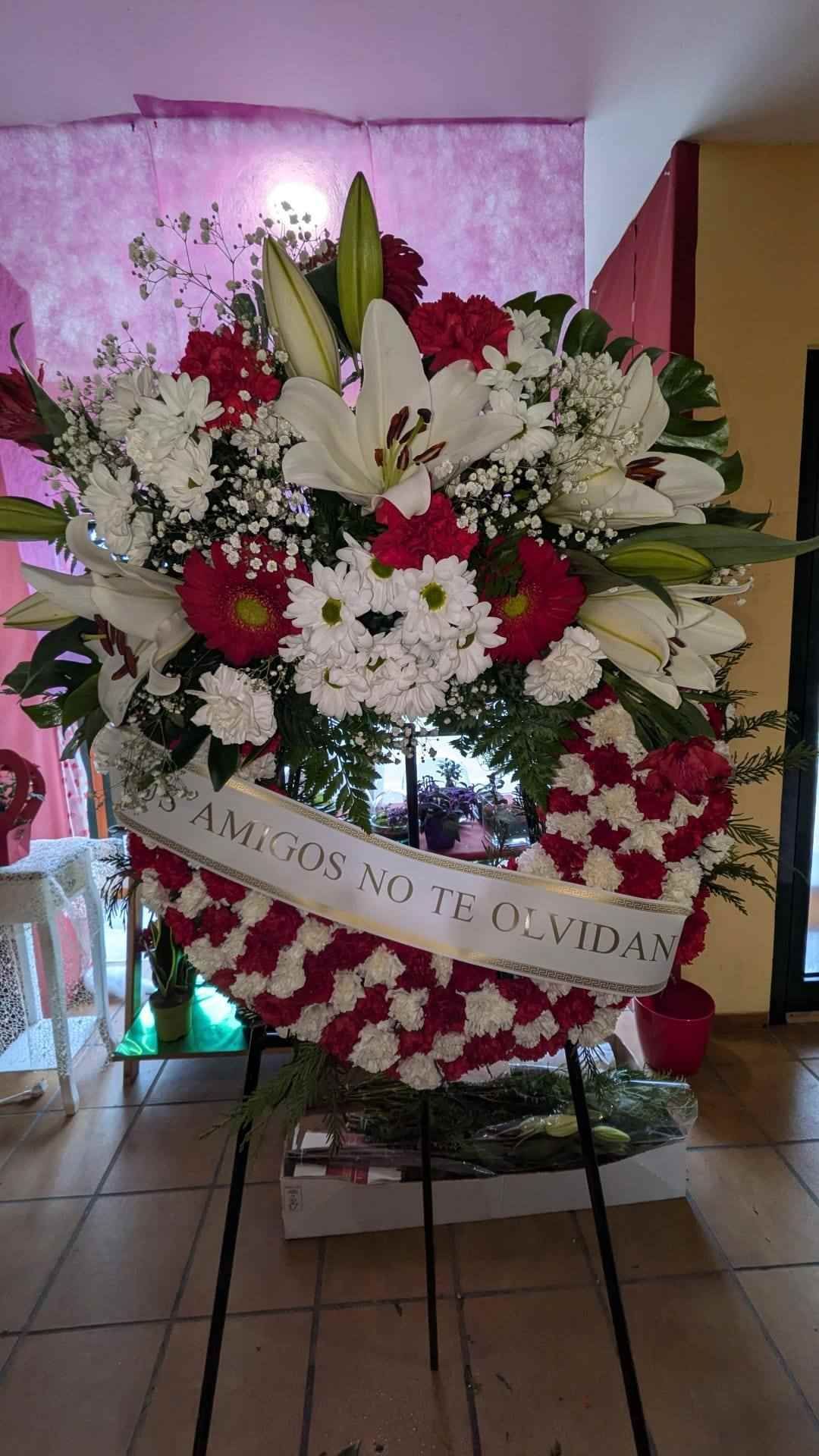 Gran corona de flores de condolencia rosas y blancas sobre un caballete con una cinta decorativa en el interior.