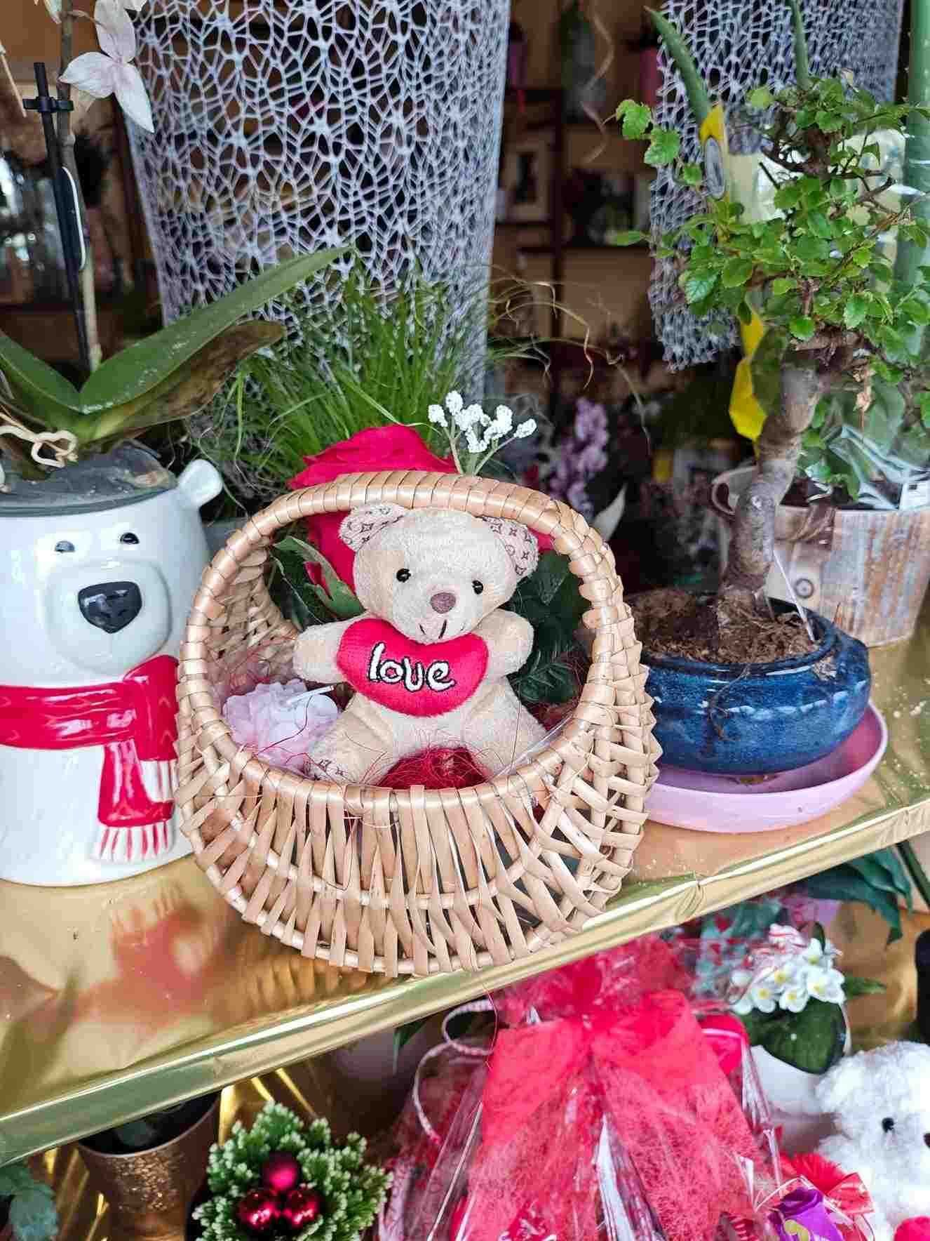 Un osito de peluche con una camiseta rosa de corazones está sentado en una cesta de mimbre