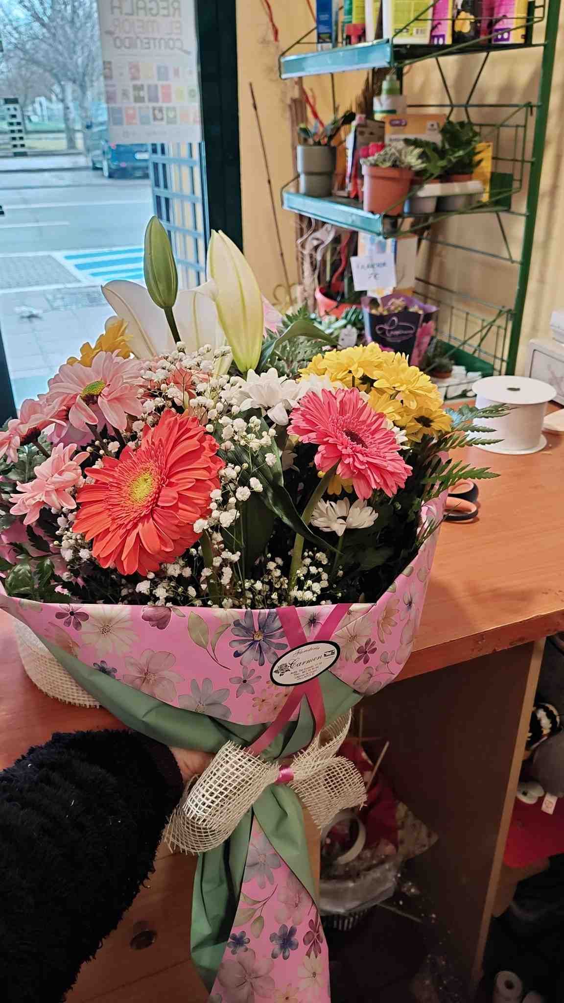 Un colorido ramo de flores envuelto en rosa sobre un mostrador de madera junto al escaparate de una tienda.