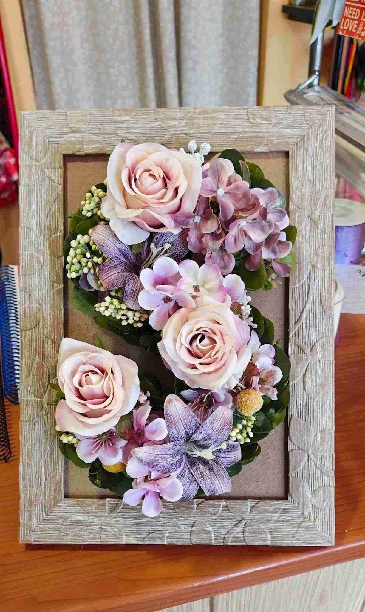 Arreglo floral enmarcado con rosas rosadas y flores moradas sobre un fondo rústico de madera.