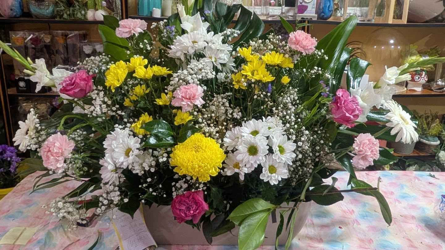 Gran ramo de flores blancas, amarillas y rosas dispuesto sobre una mesa en el interior.