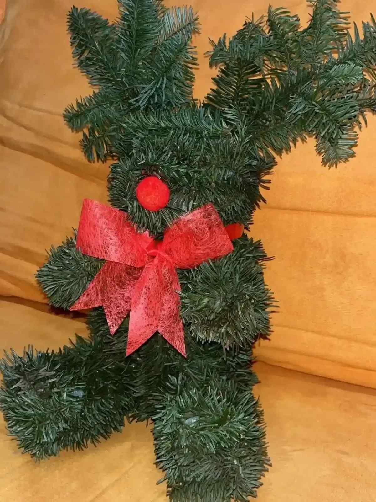 Pequeño reno verde de oropel con un lazo y nariz rojos sobre un sofá color canela.