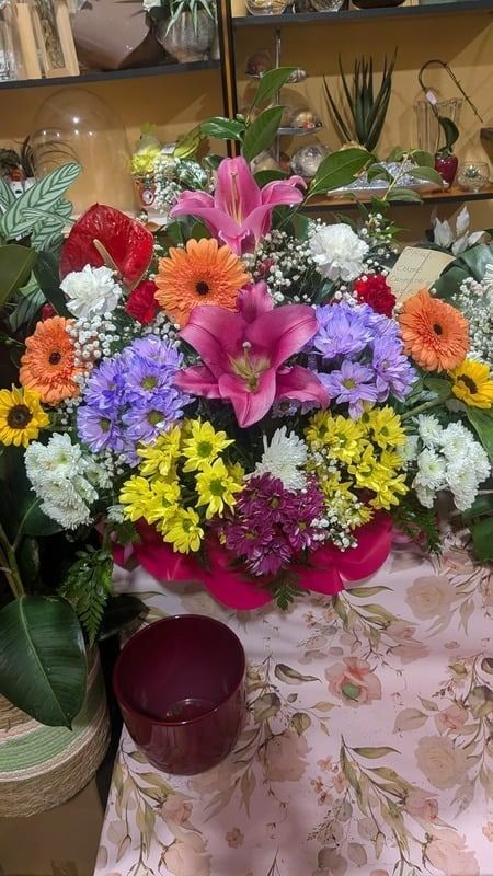 Un colorido ramo de flores variadas en un jarrón sobre una mesa, con un portavelas delante.