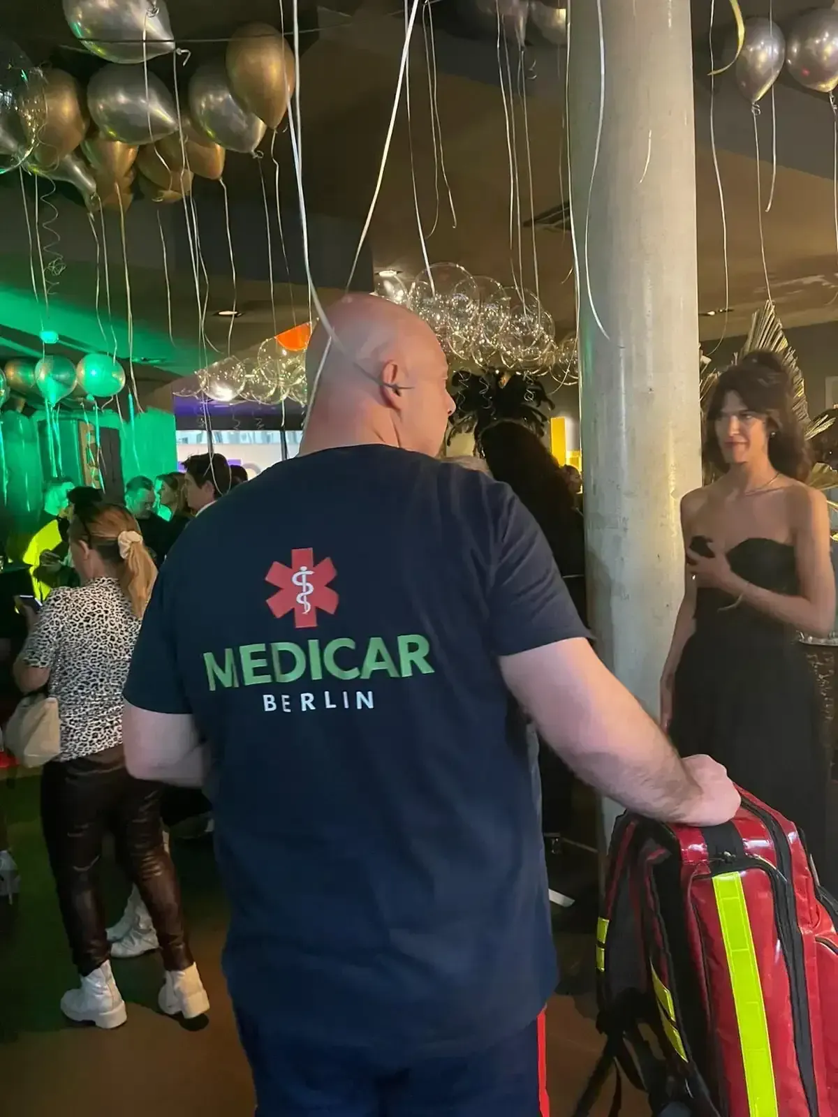 Ein Mann mit einem Medicar Berlin-Shirt steht in einem überfüllten Raum