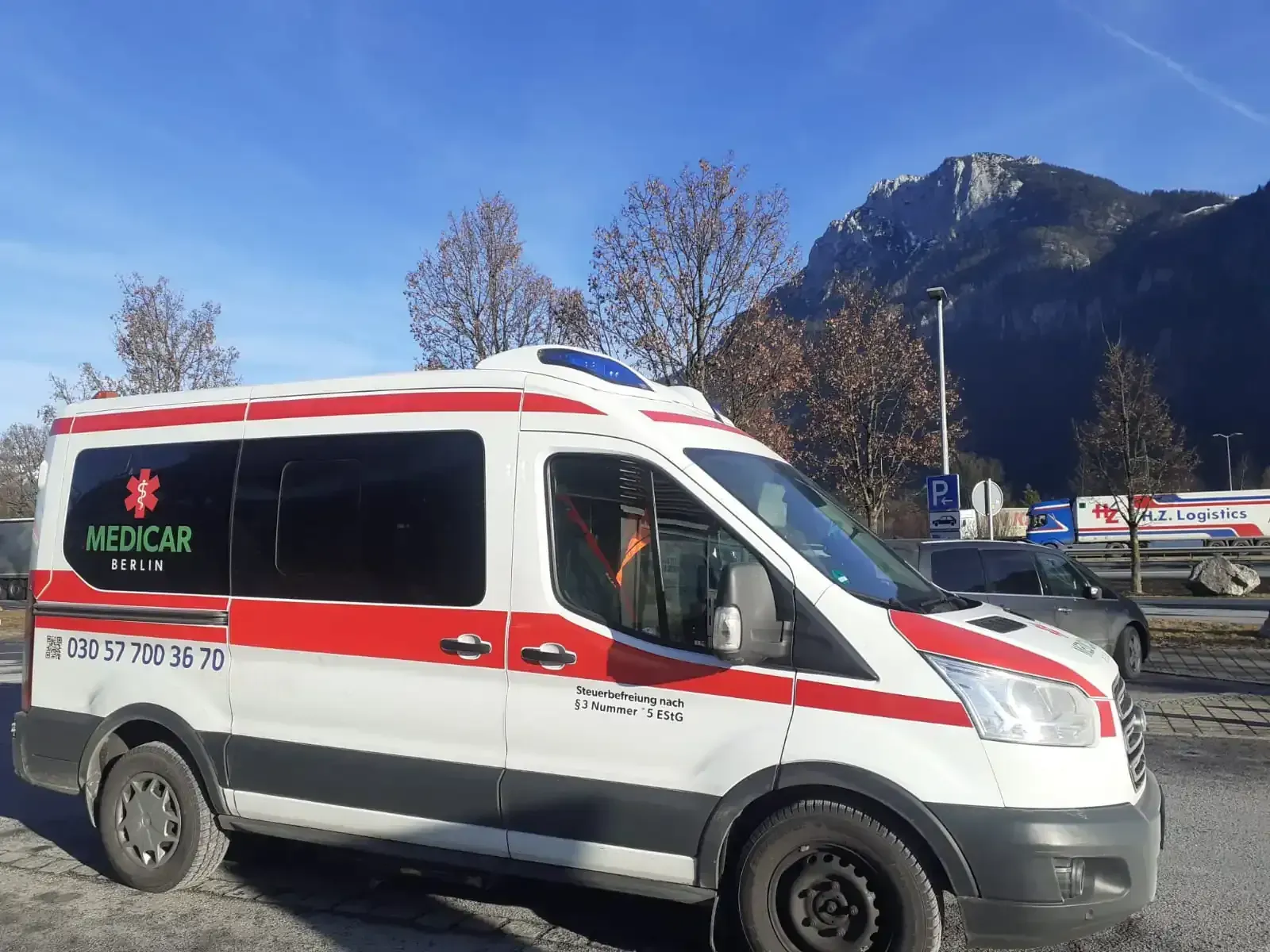Ein Krankenwagen steht auf einem Parkplatz mit Bergen im Hintergrund.