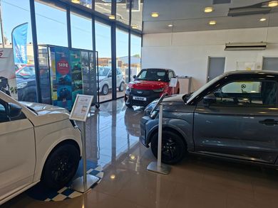 Salle d'exposition automobile avec trois voitures exposées, près de la paroi vitrée et une voiture au premier plan.