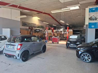 Garage de réparation automobile avec plusieurs voitures et outils à l'intérieur.