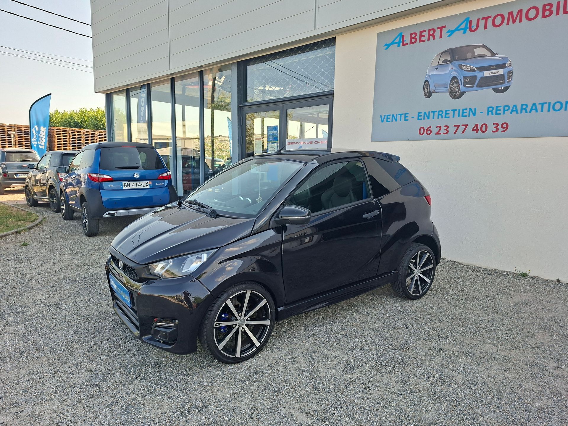 Voiture compacte garée devant un garage automobile dont le bâtiment porte une enseigne.