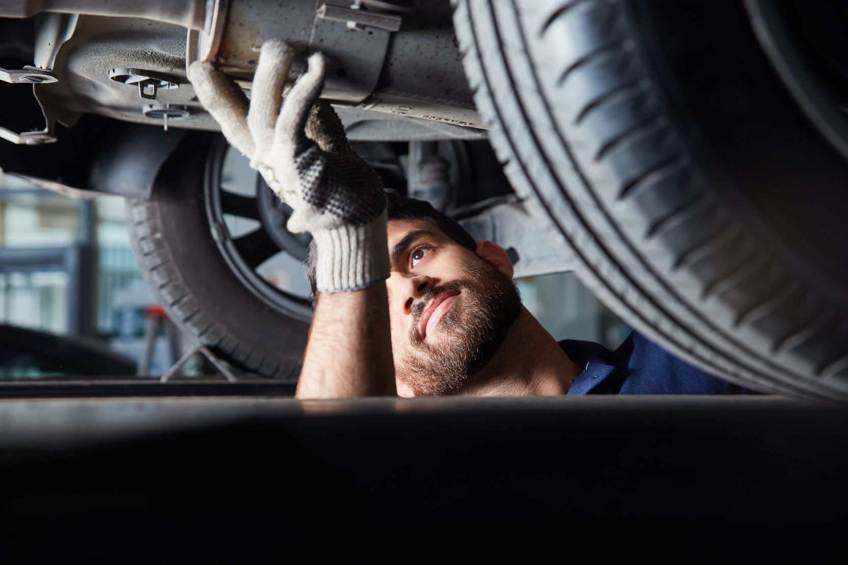 Un mécanicien inspecte le dessous d'une voiture dans un atelier, portant des gants.