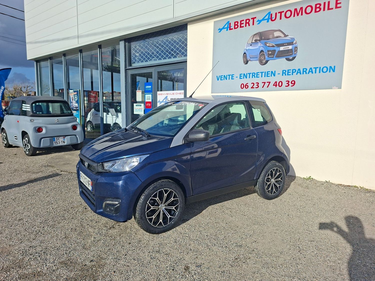 Voiture compacte garée devant un garage automobile avec une façade vitrée et une enseigne.