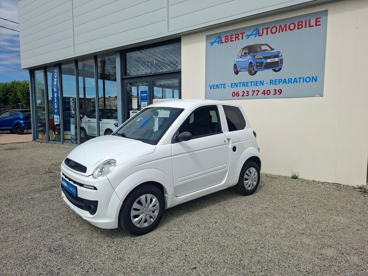 Voiture compacte garée devant un garage automobile dont le bâtiment porte une enseigne.