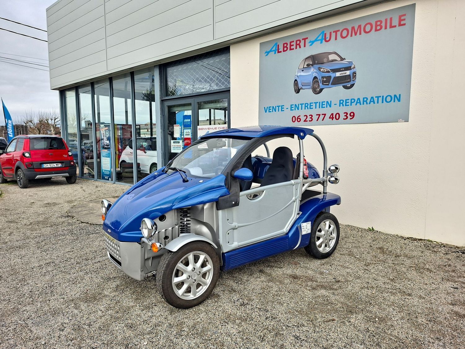 Petite voiture devant une enseigne de garage automobile.