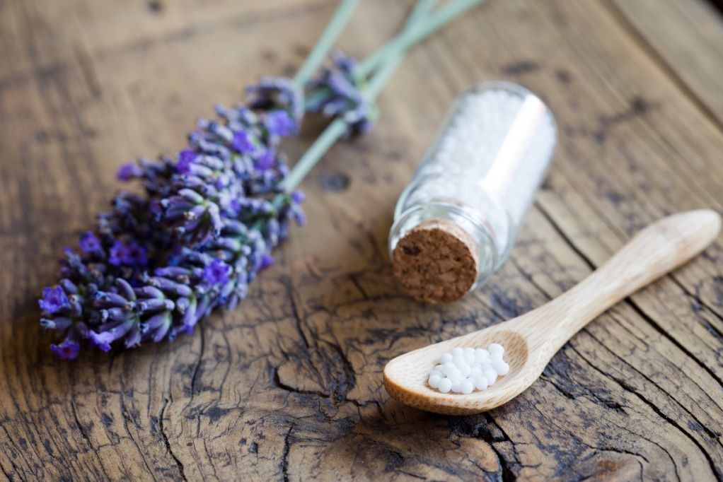 Fläschchen mit Globuli neben blühenden Pflanzen