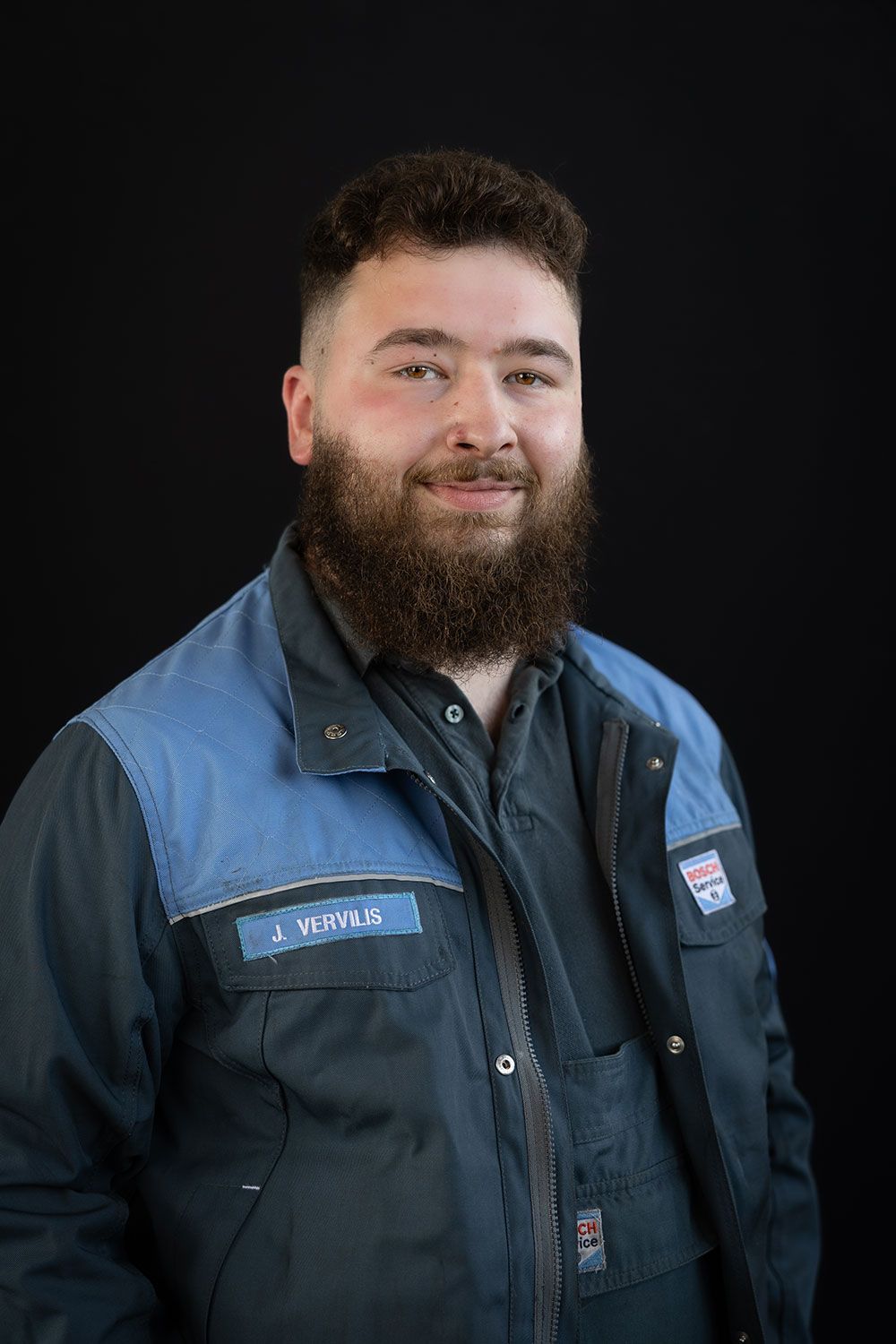 Ein Mann mit Bart trägt eine blaue Jacke und lächelt.